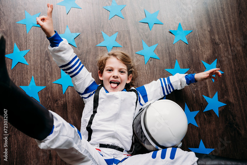 Playful girl wearing space costume lying by helmet and blue stars on floor at home photo