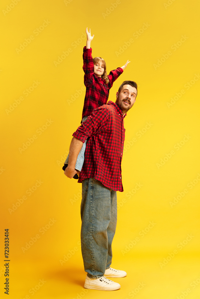 Family. Full length portrait of dad holds on back lovely daughter who very happy because have time with father against vivid yellow background. Concept of International Day of Happiness, childhood. Ad