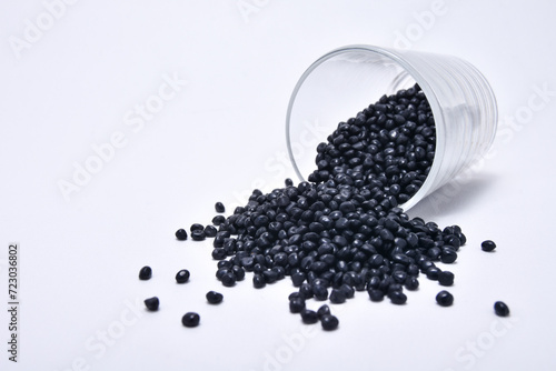 black masterbatch granules spilled from a shot glass and isolated on a white background, this polymer is a colorant for products in the plastics industry photo