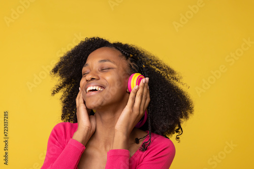 Happy young woman with eyes closed enjoying music through wireless headphones against yellow back ground photo