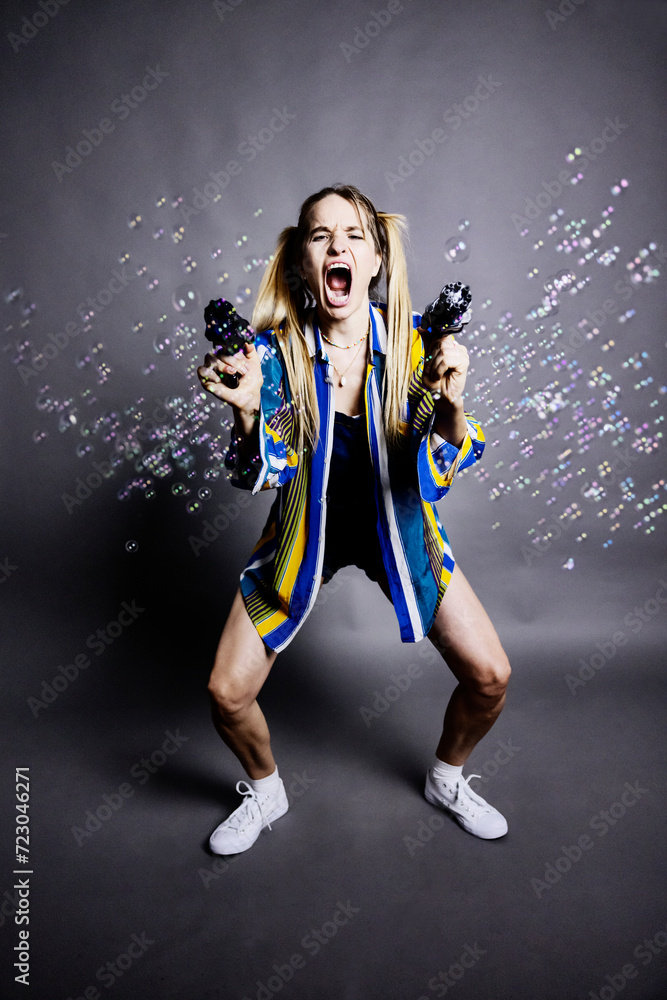 Woman shooting bubbles with guns against gray background Woman shooting bubbles with guns against gray background