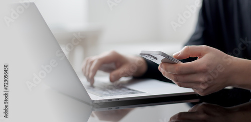 Close up of woman hand using mobile phone for online shopping and digital payment via mobile banking app. Business woman using smartphone while working on laptop computer on office table