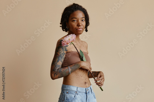 Woman with acne scars holding flower against brown background photo