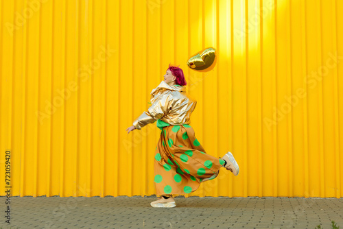 Senior woman running with heart shaped balloon in front of yellow wall