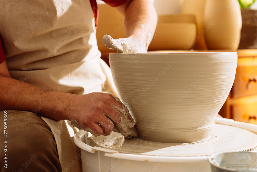 Crop of potter shaping clay pot on wheel in sunlight
