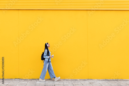 Young woman walking on footpath in front of yellow wall