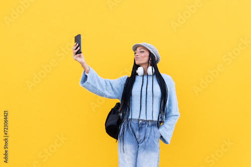 Young woman taking selfie with smart phone in front of yellow wall photo