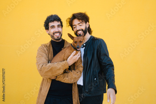 Gay couple with dog standing against yellow background photo