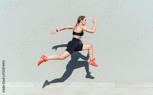 Young woman jumping by gray wall