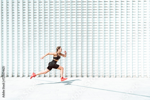 Young athlete running by white wall on sunny day