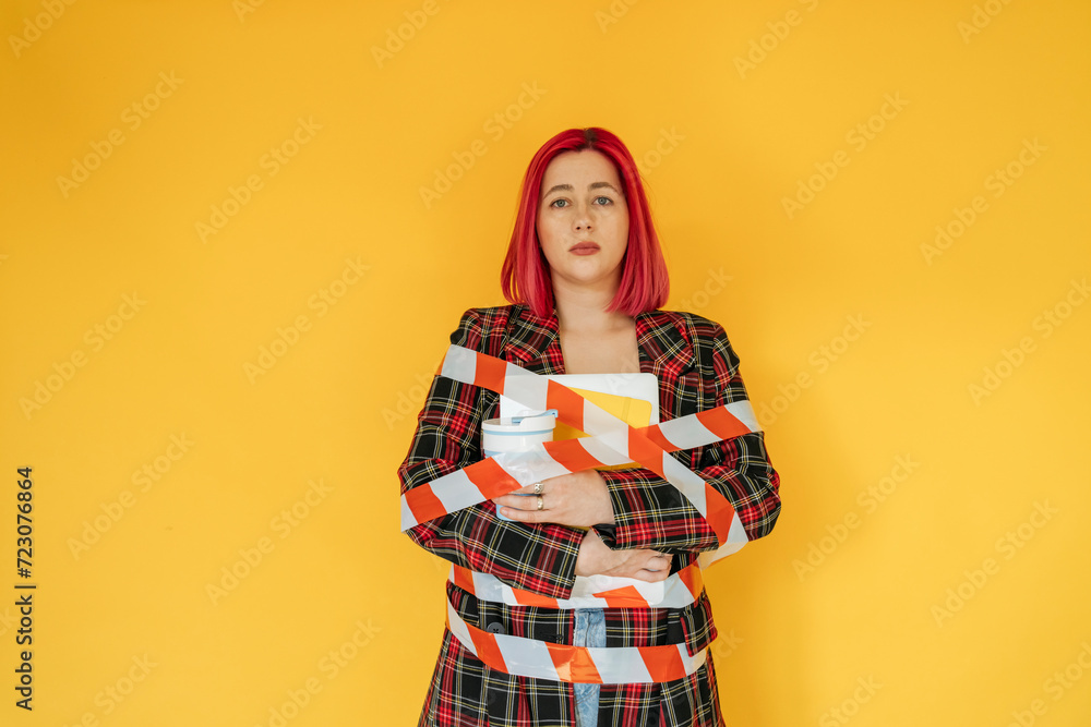 Sad woman tied with tape against yellow background Sad woman tied with tape against yellow background