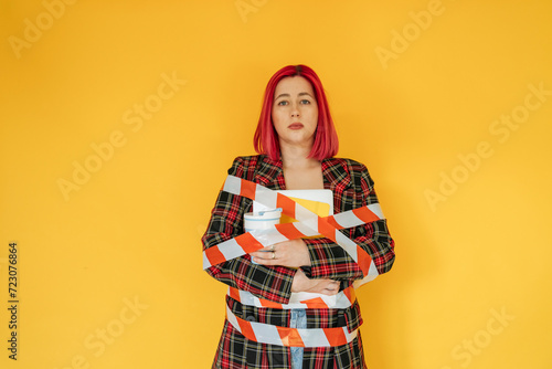 Sad woman tied with tape against yellow background