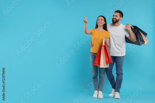 Happy couple with shopping bags looking at something on light blue background. Space for text photo