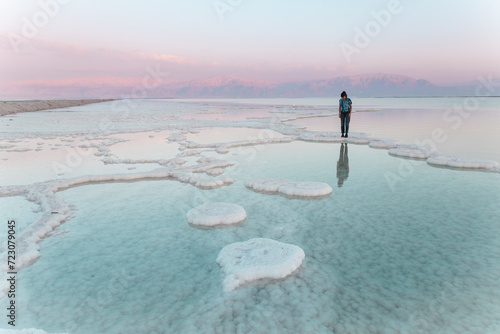 Young woman standing on salt formations in dead sea at sunset photo