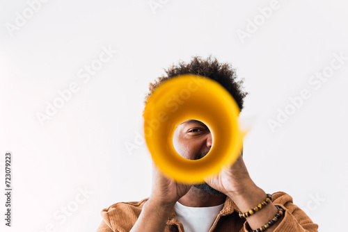 Businessman looking through rolled up yellow paper in front of white wall photo