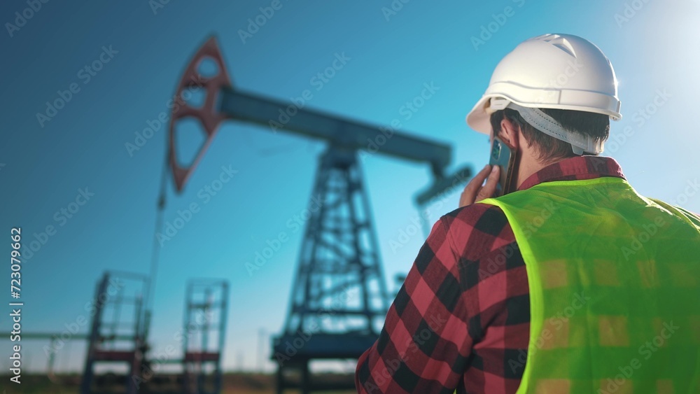 oil business. a worker works next to an oil pump and inspecting it. industry business oil and gas concept. engineer studying oil production and talking on the phone lifestyle with a colleague