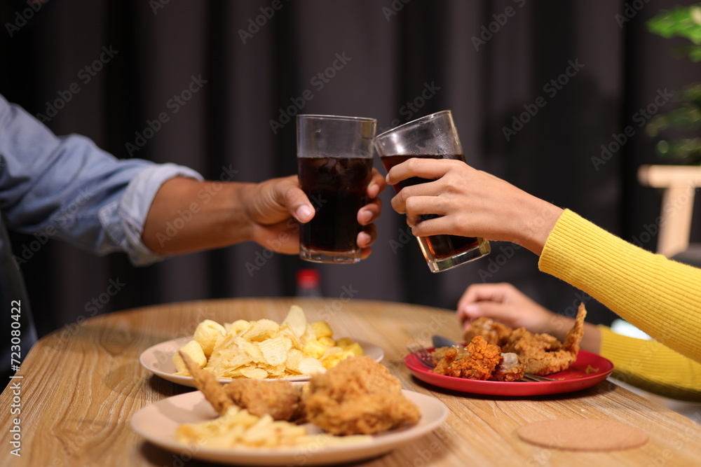 Young man and woman are eating dinner together at home. Friends eating fried chicken, drinks and snacks together while having dinner at home.