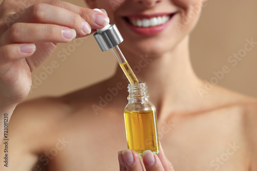 Woman with cosmetic serum in her hands on beige background, closeup