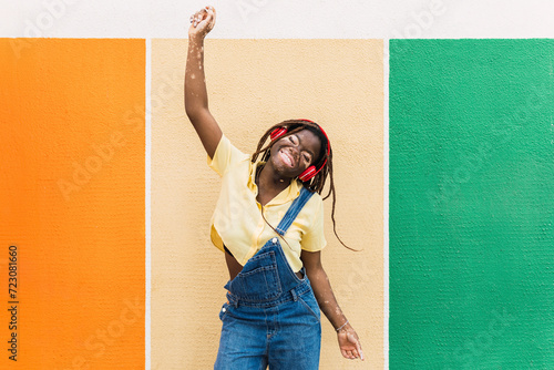 Happy young woman wearing wireless headphones dancing in front of multi colored wall photo