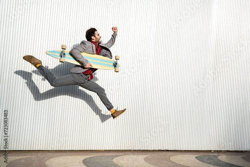 Businessman with long board jumping by wall on footpath photo