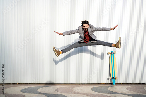 Cheerful man with doing splits while jumping on footpath in front of wall photo