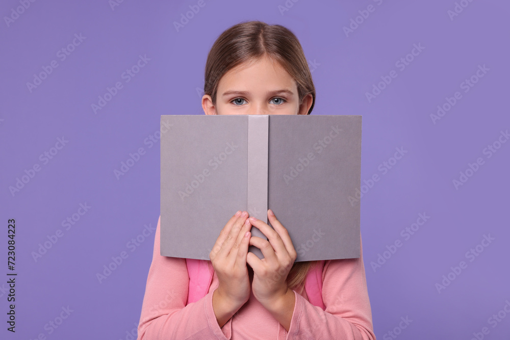 Cute schoolgirl with open book on violet background