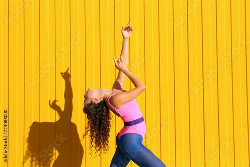 Young woman wearing bodysuit dancing in front of yellow wall photo