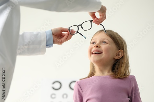 Vision testing. Ophthalmologist giving glasses to little girl indoors, low angle view photo