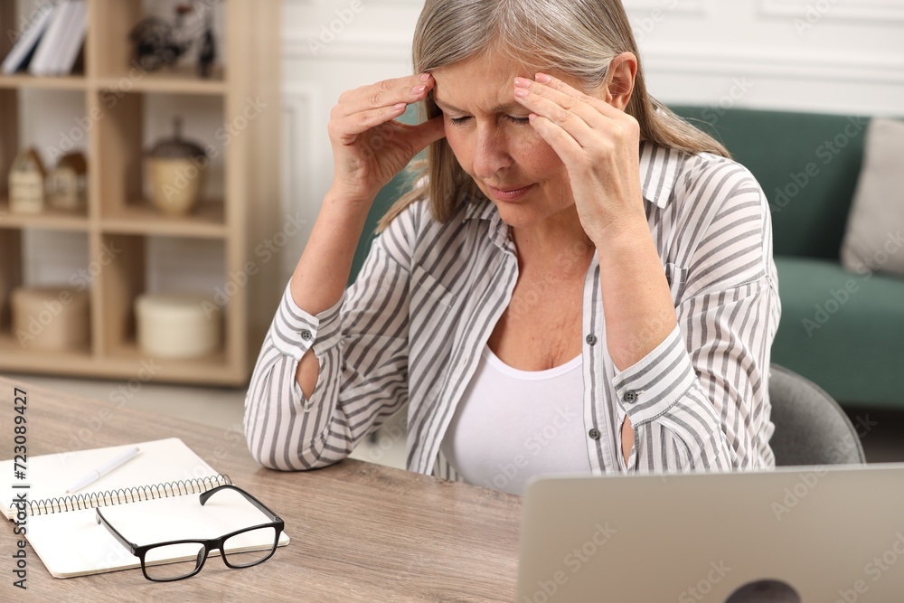 Menopause. Woman suffering from headache at wooden table indoors Menopause. Woman suffering from headache at wooden table indoors
