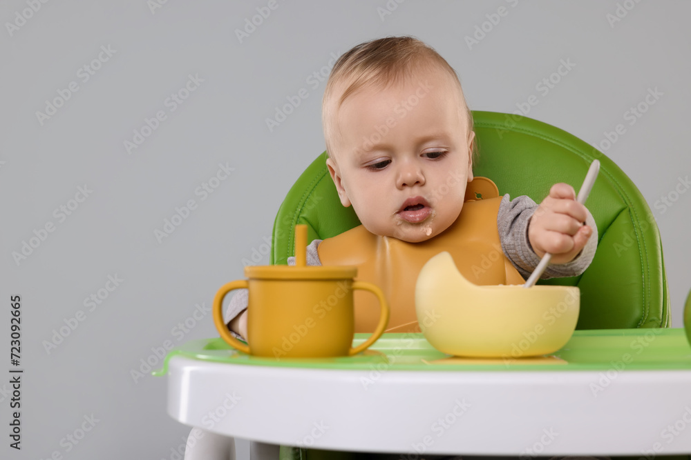Cute little baby eating healthy food in high chair on gray background, space for text Cute little baby eating healthy food in high chair on gray background, space for text