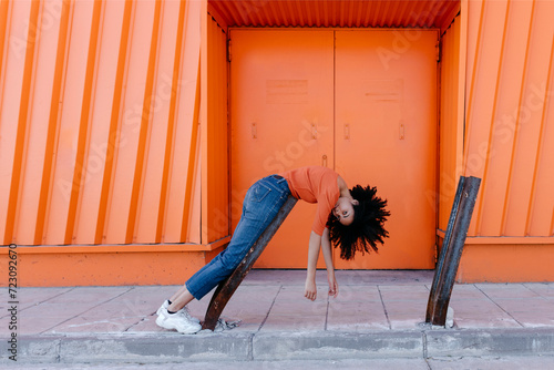 Young afro woman leaning on metal by orange door photo