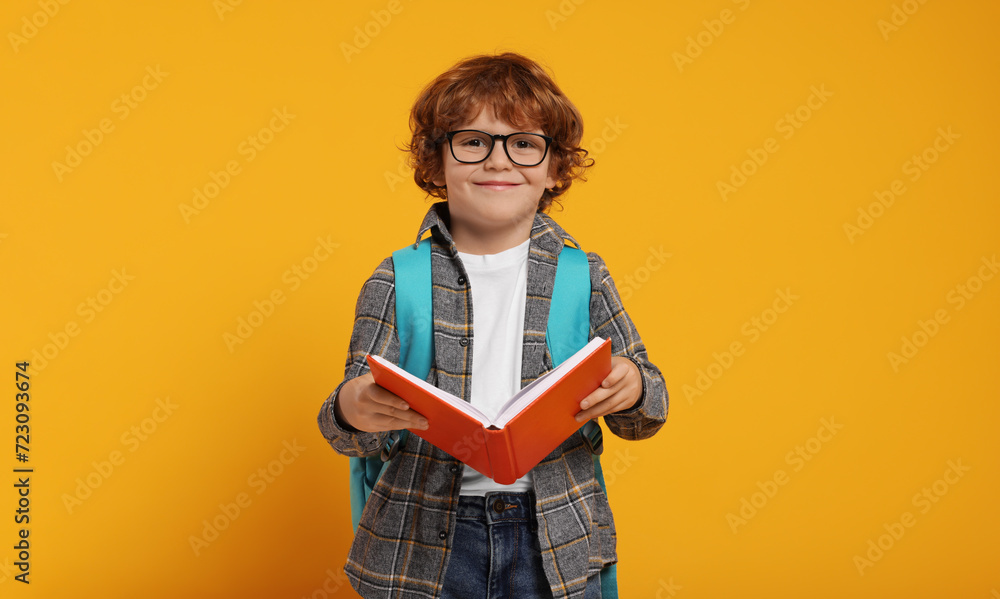 Happy schoolboy with backpack and book on orange background, space for text Happy schoolboy with backpack and book on orange background, space for text
