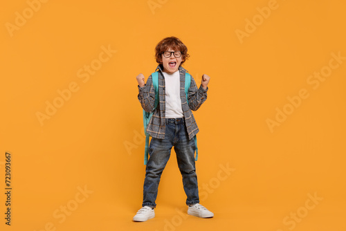 Emotional schoolboy with backpack on orange background