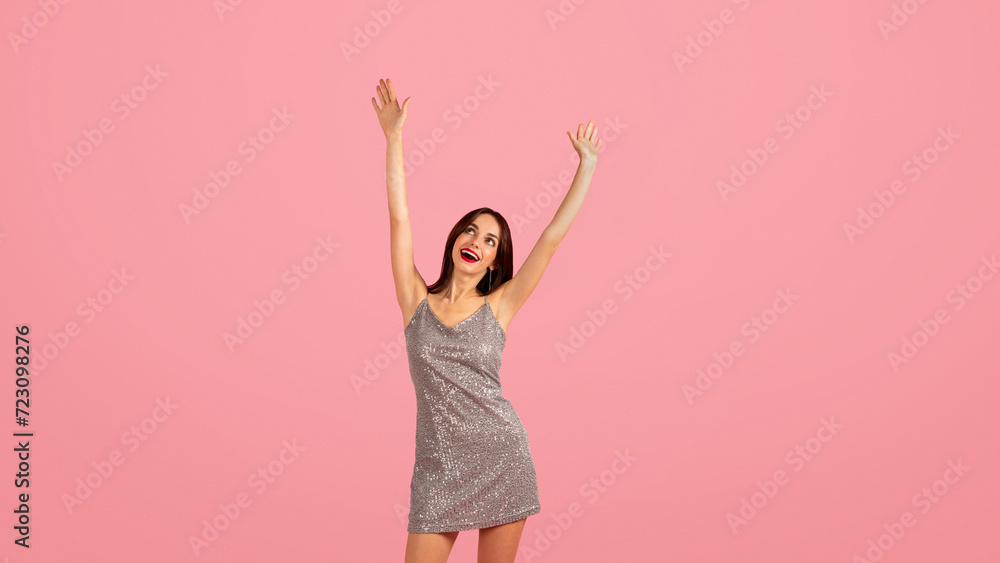 Exuberant young woman in a sparkling silver dress joyfully raises her hands up in the air Exuberant young woman in a sparkling silver dress joyfully raises her hands up in the air