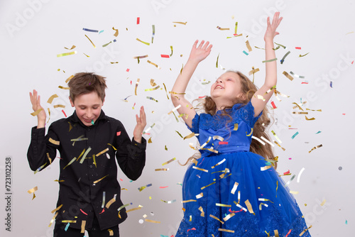 Happy party. Small handsome boy and his little pretty sister wearing cone caps laughing and throwing colorful confetti isolated on white background