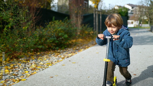 Joyful Three-Year-Old Boy Riding Toy Scooter Outdoors in Autumn Sunshine