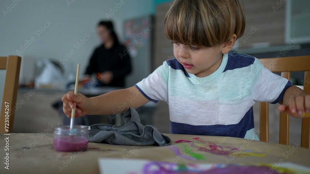 Little boy cleaning brush with water at home during painting session. Creative kid rinsing brush inside glass cup with water Little boy cleaning brush with water at home during painting session. Creative kid rinsing brush inside glass cup with water