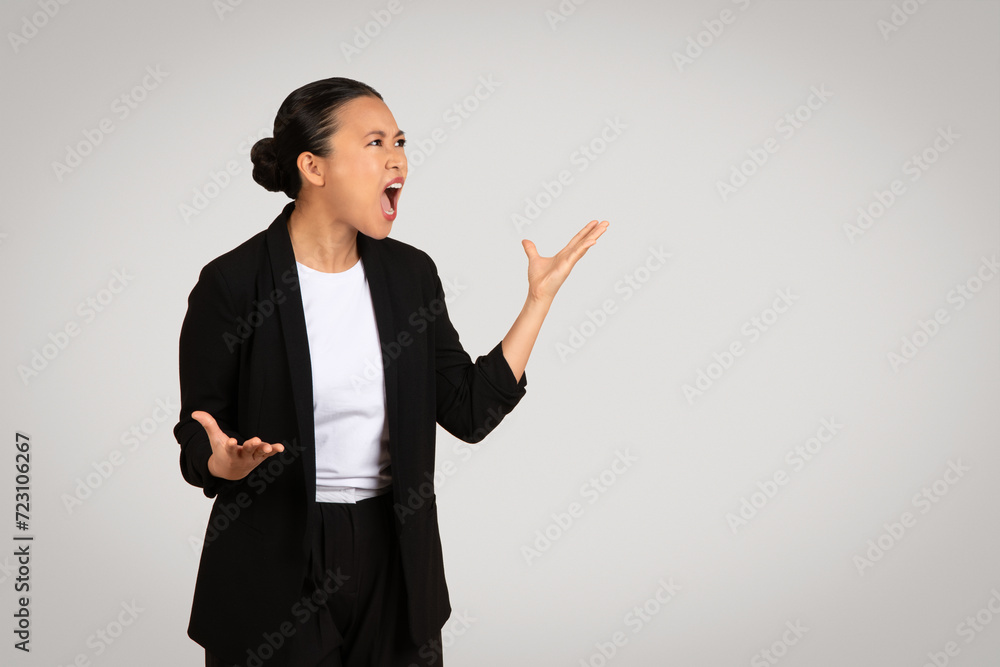 Animated Asian businesswoman in professional attire shouting and gesturing with hands Animated Asian businesswoman in professional attire shouting and gesturing with hands