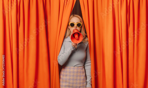 Woman talking through megaphone standing amidst orange curtains photo