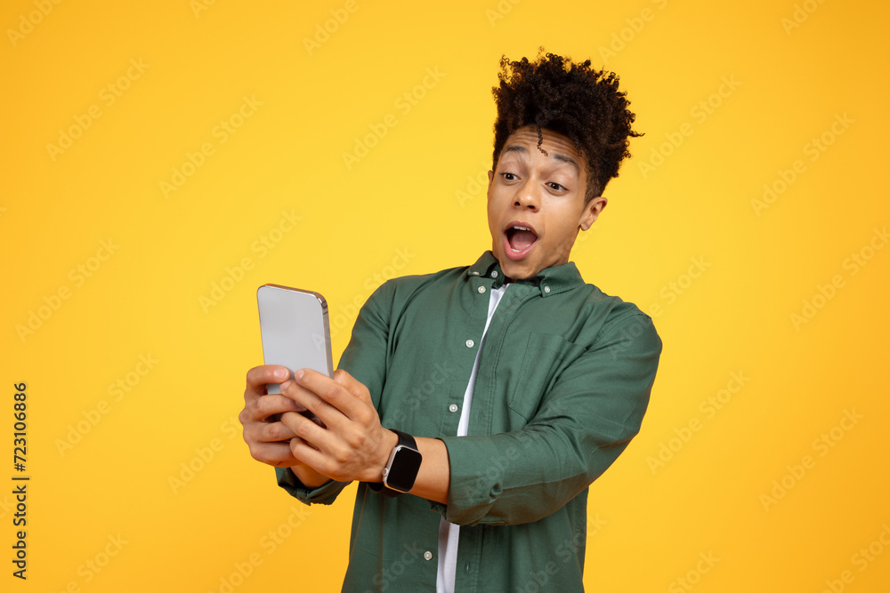 Amazed african american guy looking at smartphone screen Amazed african american guy looking at smartphone screen