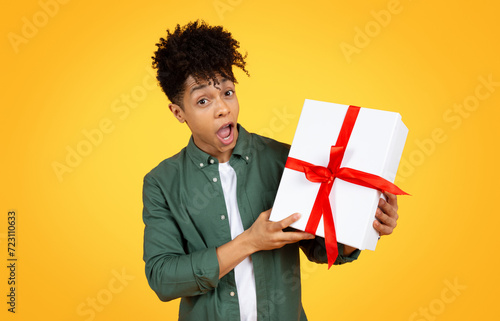 Amazed young african american guy holding gift box photo
