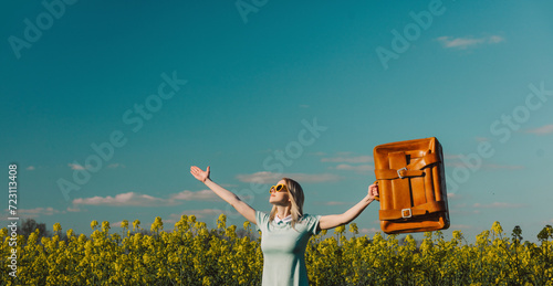 Carefree woman with suitcase standing in rapeseed field photo