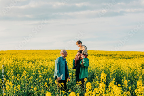 Father carrying son on shoulder next to grandfather in rapeseed field photo