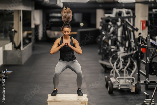 A sporty woman is jumping on a box and exercising in a gym.