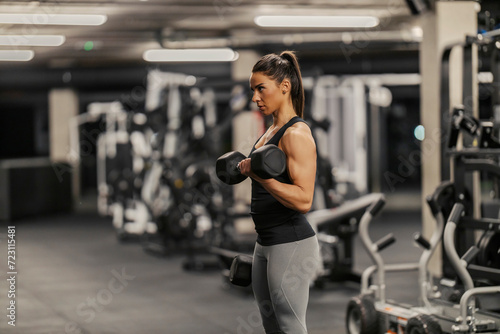 A strong sportswoman is lifting workouts with dumbbell in a gym.