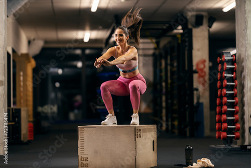 A happy sportswoman is jumping on a jump box in a gym with heart rate belt.