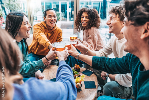 Group of young people enjoying happy hour sitting at bar table - Happy multiracial friends cheering beer glasses at brewery pub - Life style concept with guys and girls having dinner party together photo