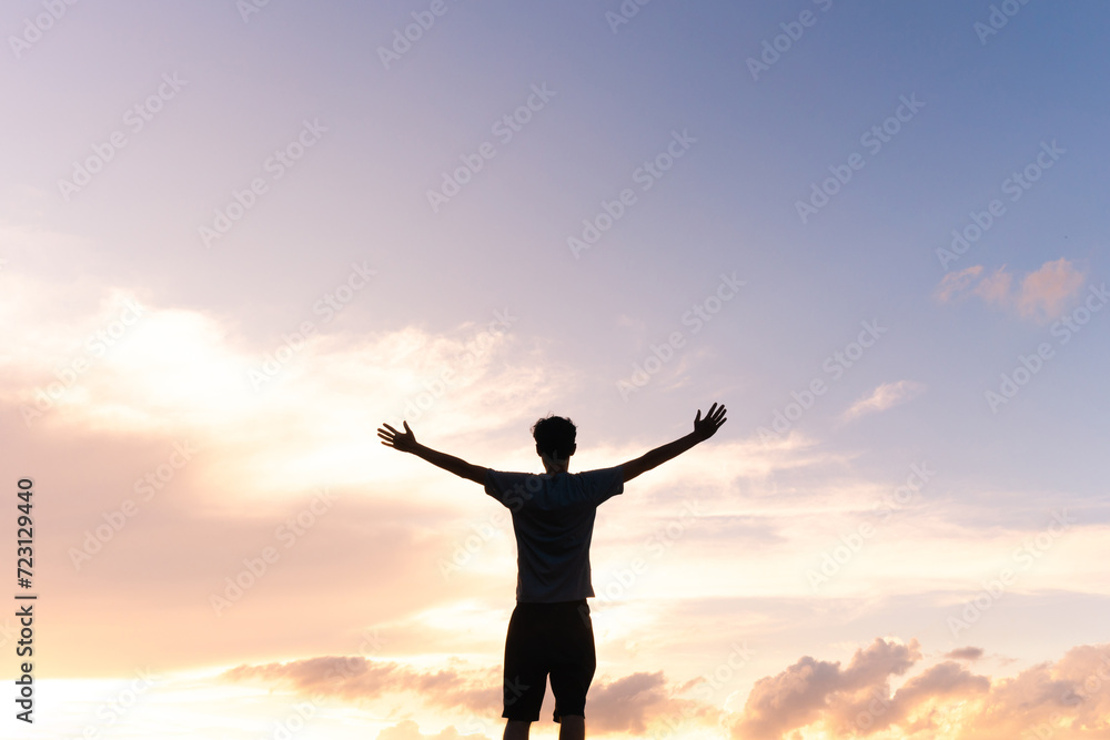 Silhouette of a man with arms open against a beautiful sky, expressing gratitude for success and happiness