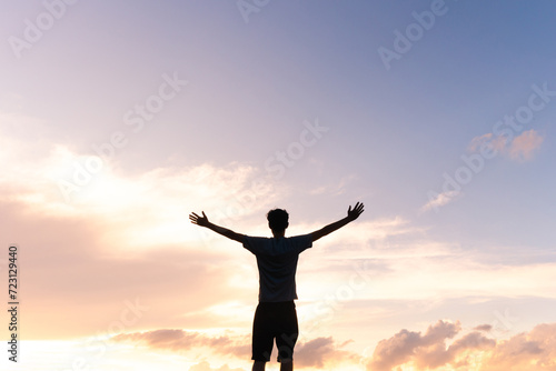 Silhouette of a man with arms open against a beautiful sky, expressing gratitude for success and happiness