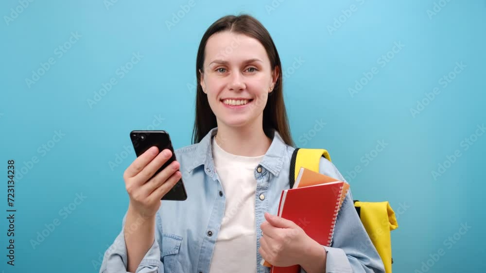 Portrait of excited woman student in shirt with backpack hold notebooks using mobile cell phone typing sms message, isolated over blue background. Education in high school university college concept Portrait of excited woman student in shirt with backpack hold notebooks using mobile cell phone typing sms message, isolated over blue background. Education in high school university college concept